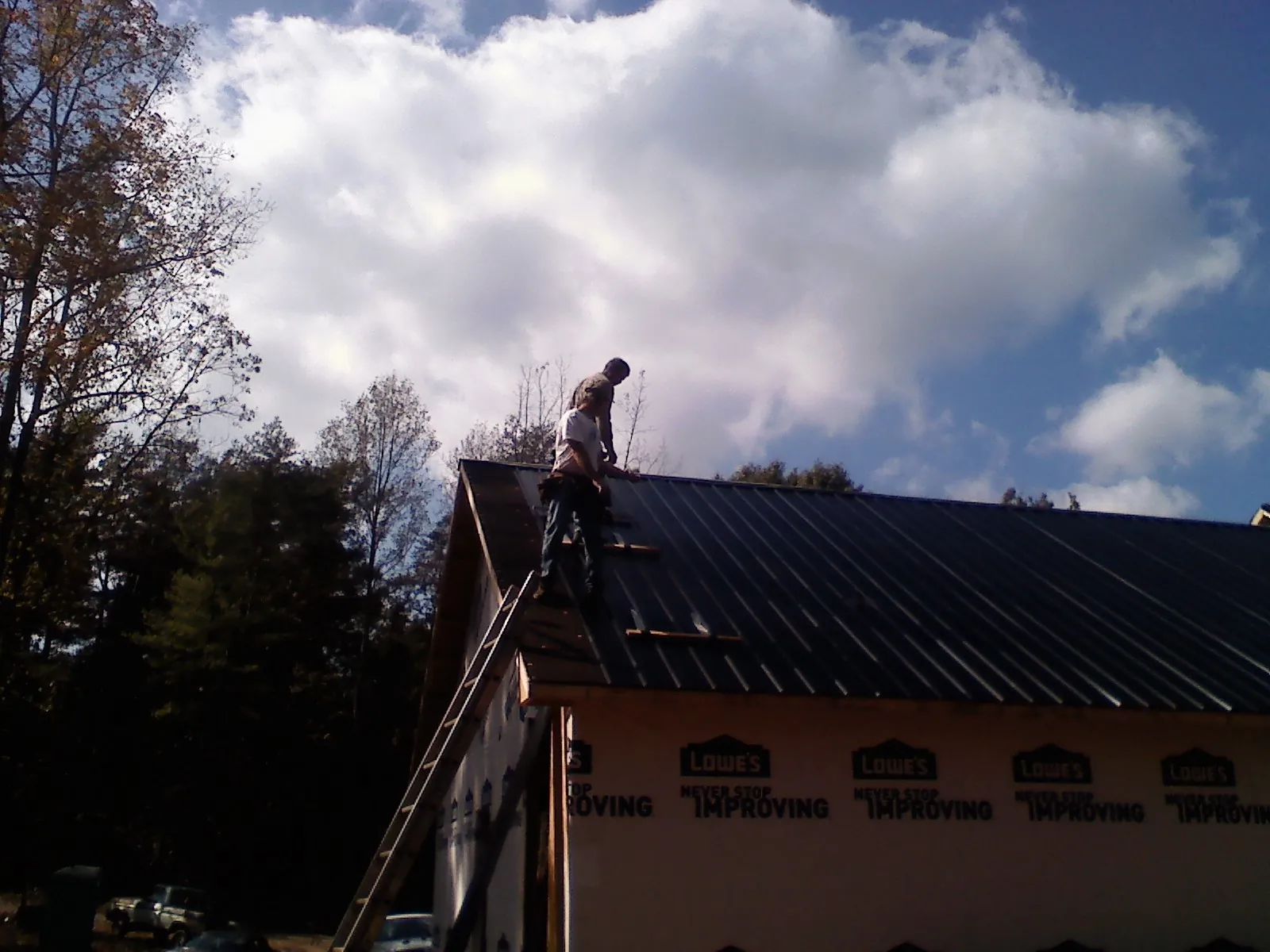 Roofer fastening dark metal panels high against a cloudy sky, from a Roof Inspection job in Tuscarora